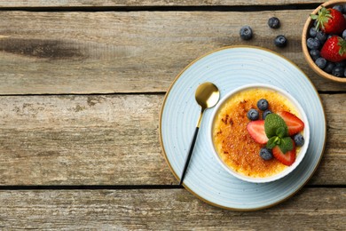 Delicious creme brulee with berries and mint in bowl served on wooden table, flat lay. Space for text