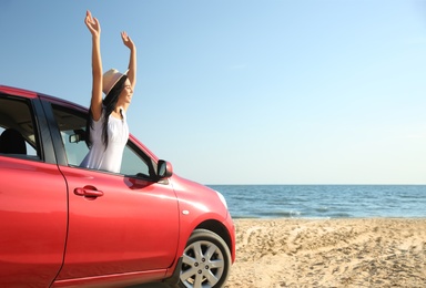 Photo of Happy young woman leaning out of car window on beach, space for text. Summer trip