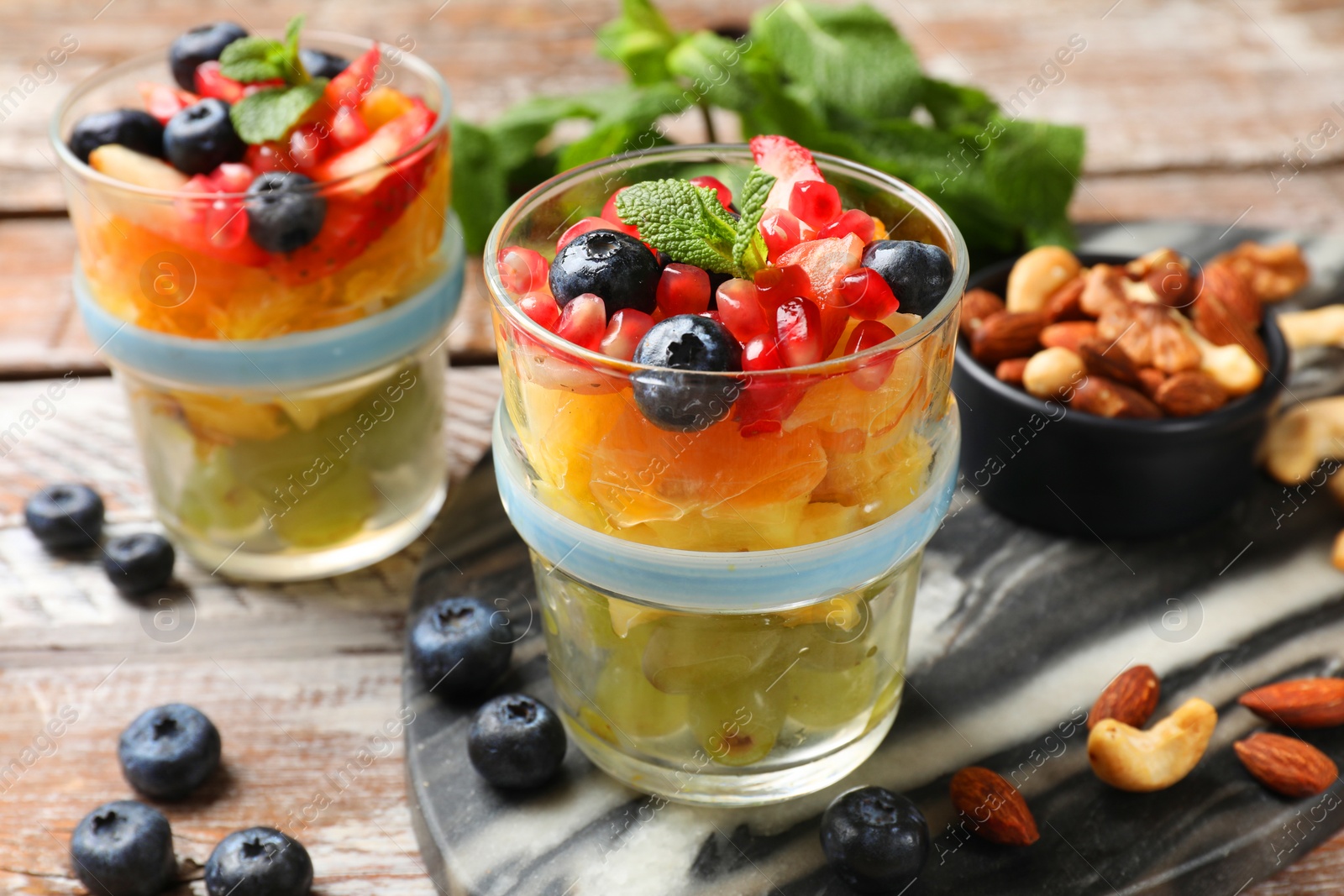 Photo of Delicious fruit salad, fresh berries, mint and nuts on wooden table