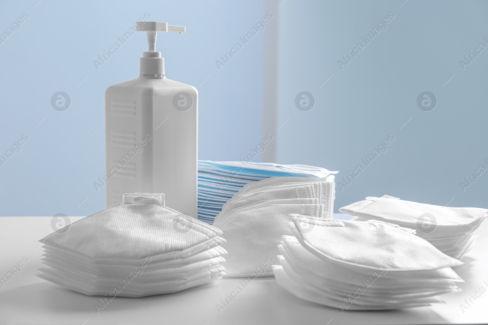 Photo of Hand sanitizer and respiratory masks on table against white background. Protective essentials during COVID-19 pandemic