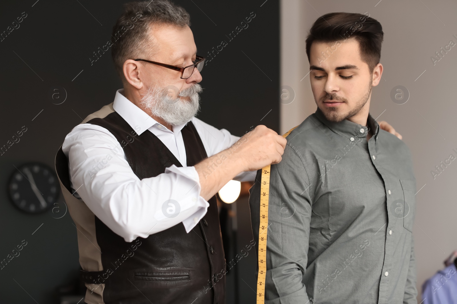 Photo of Mature tailor taking client's measurements in atelier