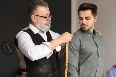 Photo of Mature tailor taking client's measurements in atelier