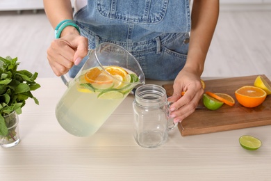 Photo of Young woman pouring lemonade into mason jar on table, closeup. Natural detox drink