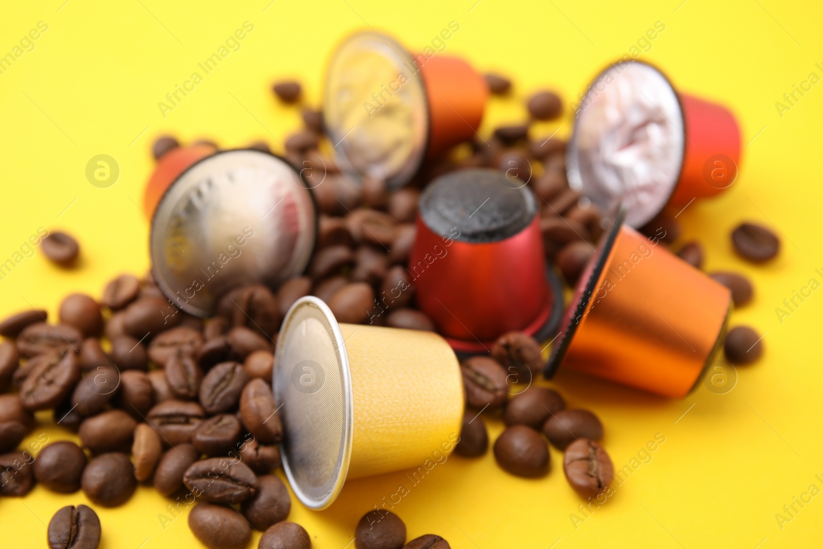 Photo of Many coffee capsules and beans on yellow background, closeup
