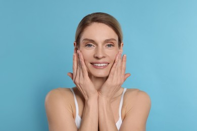 Woman massaging her face on turquoise background