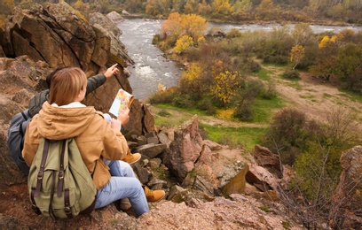 Photo of Couple of travelers with backpacks and map sitting on steep cliff. Autumn vacation
