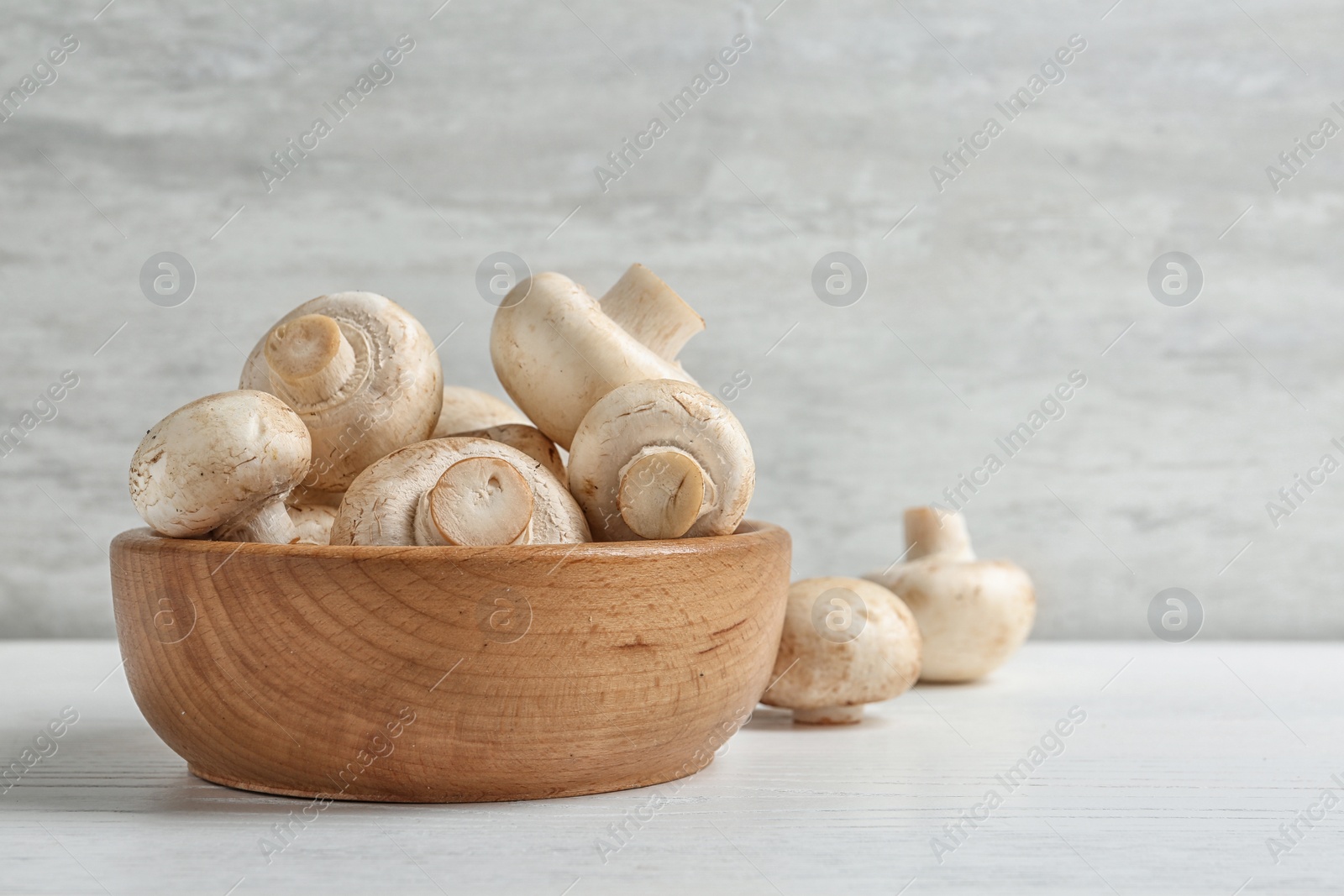 Photo of Bowl with fresh champignon mushrooms on wooden table, space for text