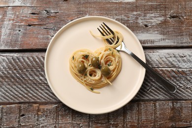 Photo of Heart made of tasty spaghetti, fork, olives and cheese on wooden table, top view