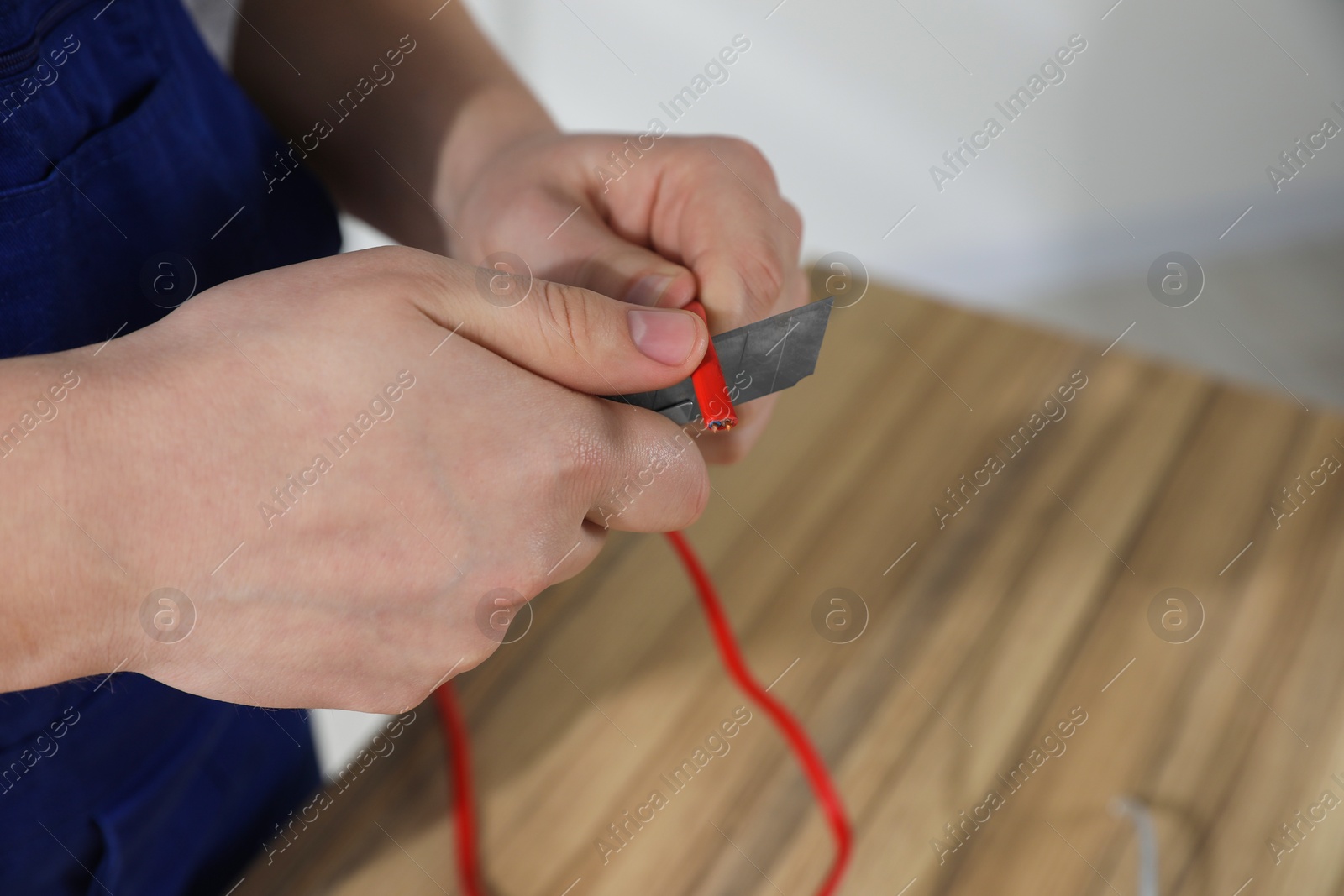 Photo of Professional electrician in uniform stripping wiring indoors, closeup