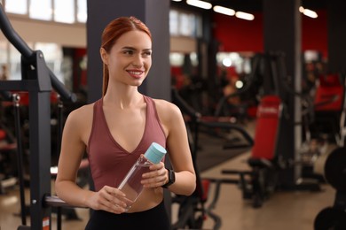 Photo of Athletic young woman with bottle of water in gym, space for text