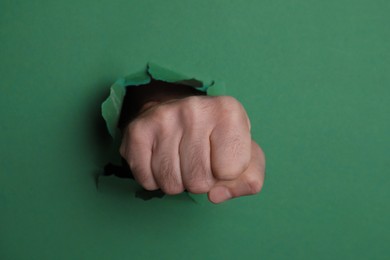 Man breaking through green paper with fist, closeup