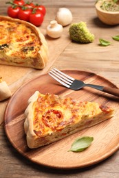 Piece of delicious homemade vegetable quiche and fork on wooden plate