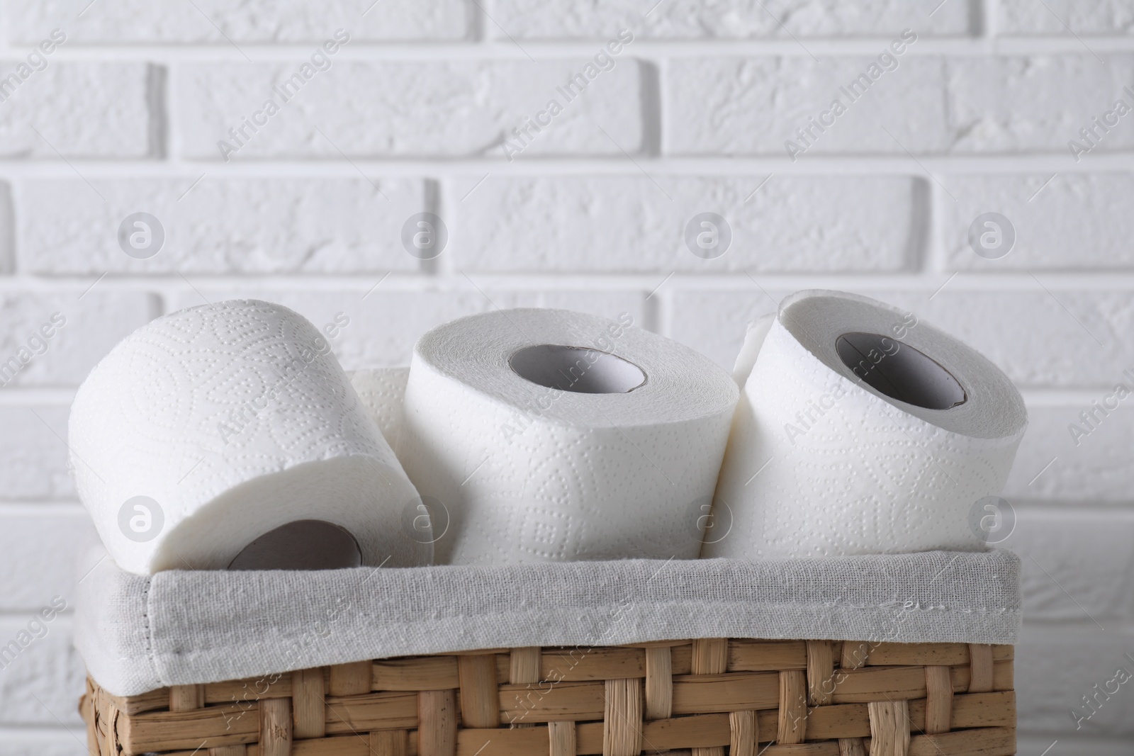 Photo of Toilet paper rolls in wicker basket against white brick wall