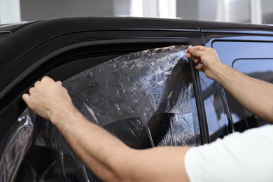 Photo of Worker tinting car window with foil in workshop, closeup