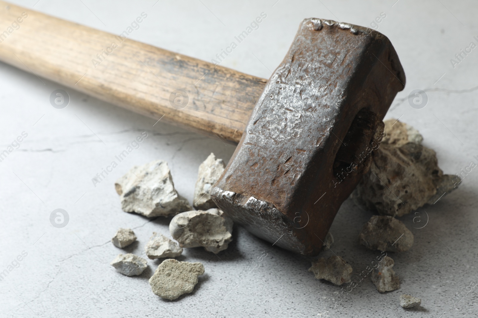 Photo of One sledgehammer and pieces of broken stones on grey textured background, closeup