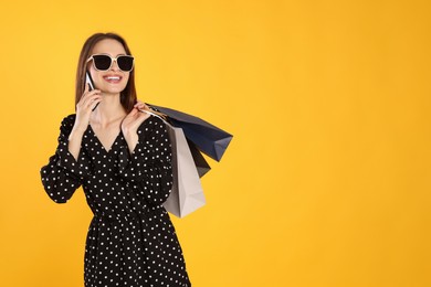 Photo of Happy young woman with shopping bags and smartphone on yellow background. Big sale