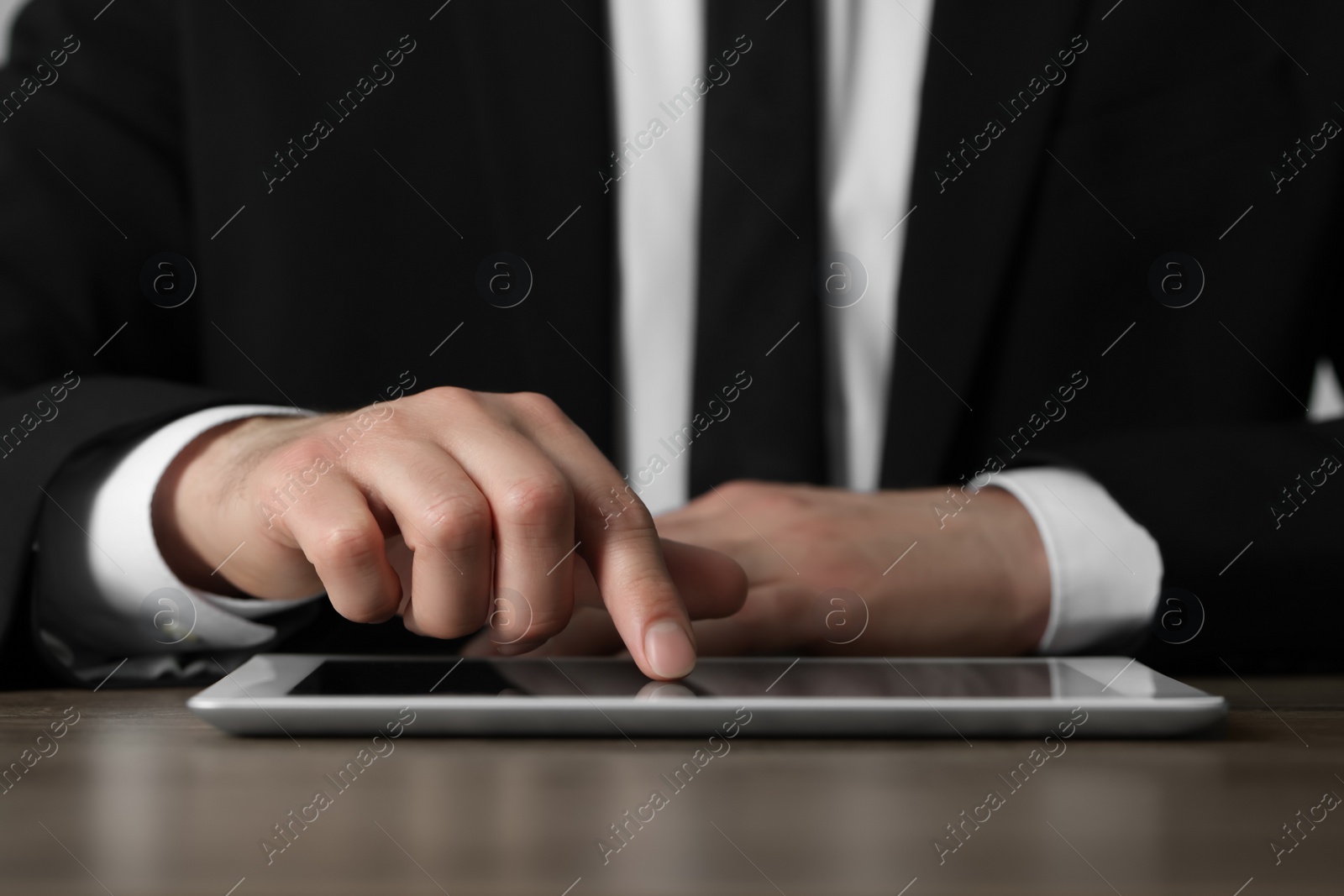 Photo of Closeup view of man using new tablet at wooden desk indoors