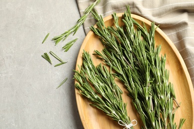 Photo of Wooden plate with fresh rosemary twigs on table, top view