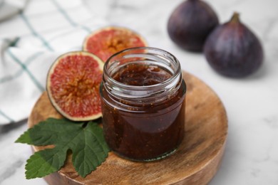 Photo of Glass jar of tasty sweet fig jam and fruits on white marble table