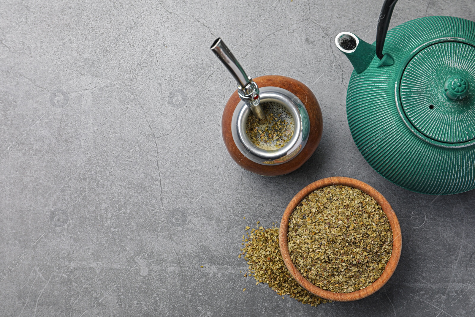 Photo of Calabash with bombilla, teapot and bowl of mate tea leaves on grey table, flat lay. Space for text