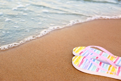 Photo of Stylish flip flops on sand near sea, space for text. Beach accessories