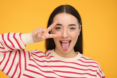Photo of Happy woman showing her tongue and V-sign on orange background