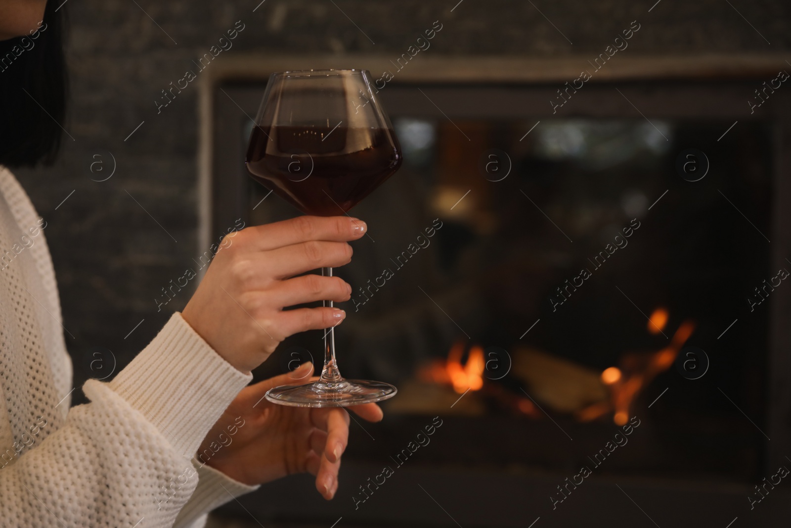 Photo of Woman with glass of wine near burning fireplace, closeup. Space for text