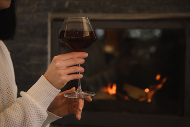 Woman with glass of wine near burning fireplace, closeup. Space for text