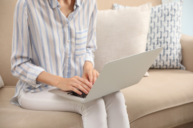 Photo of Young woman with laptop sitting on sofa indoors, closeup