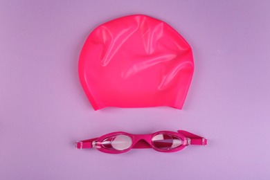 Photo of Swim goggles and cap on violet background, flat lay