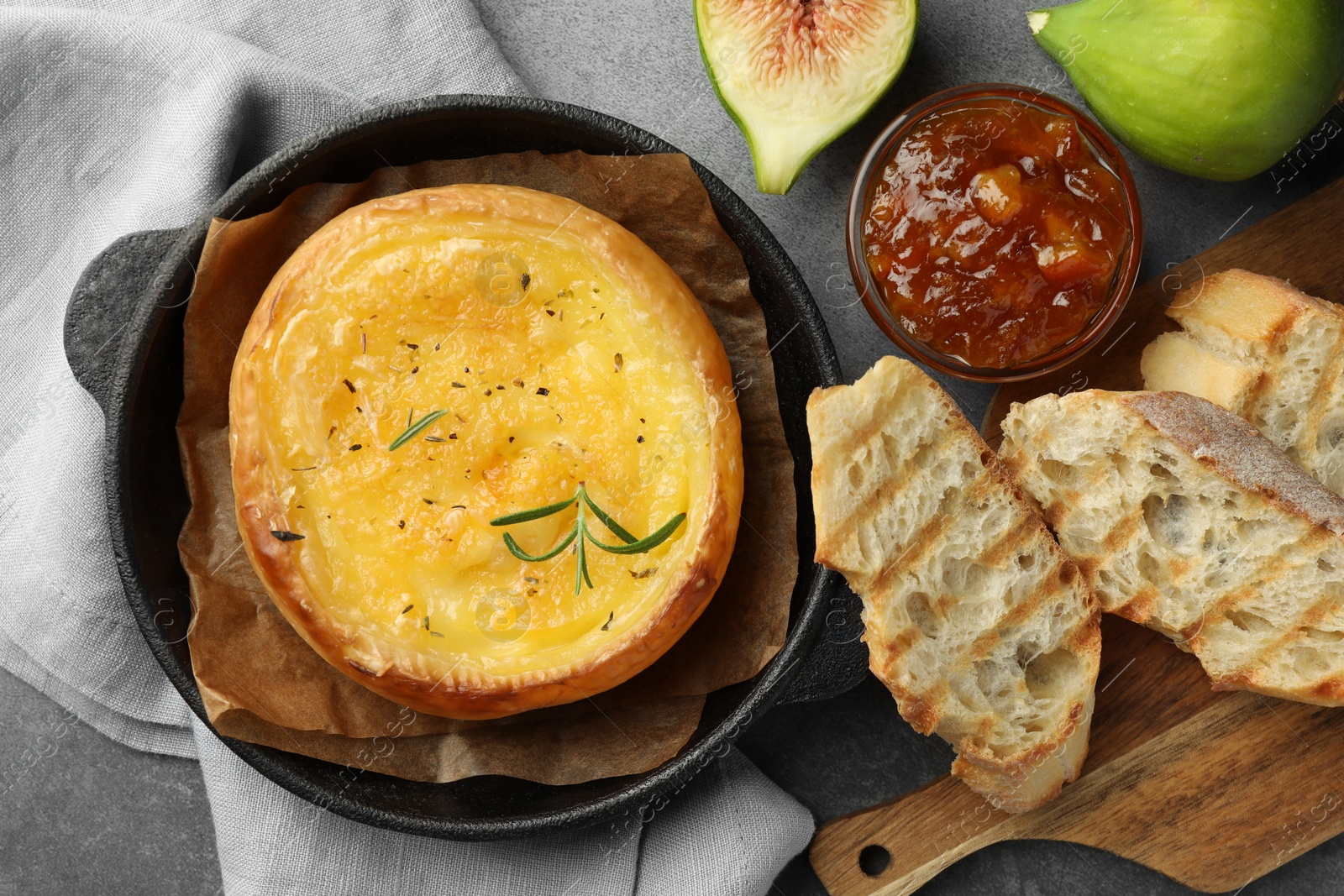 Photo of Tasty baked brie cheese and products on grey table, flat lay