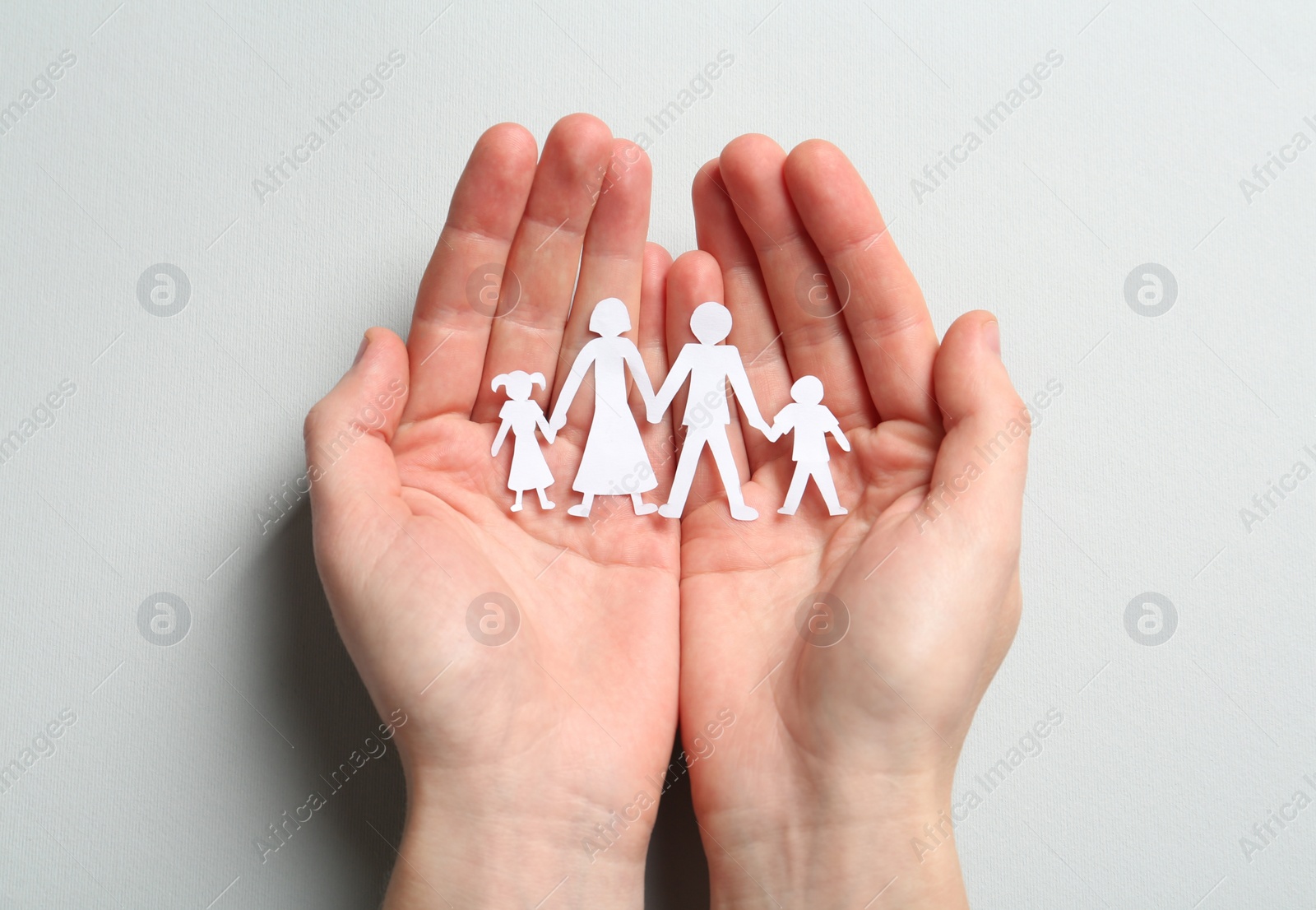 Photo of Woman holding paper cutout of family on light background, top view