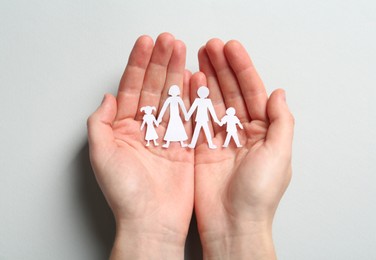 Woman holding paper cutout of family on light background, top view