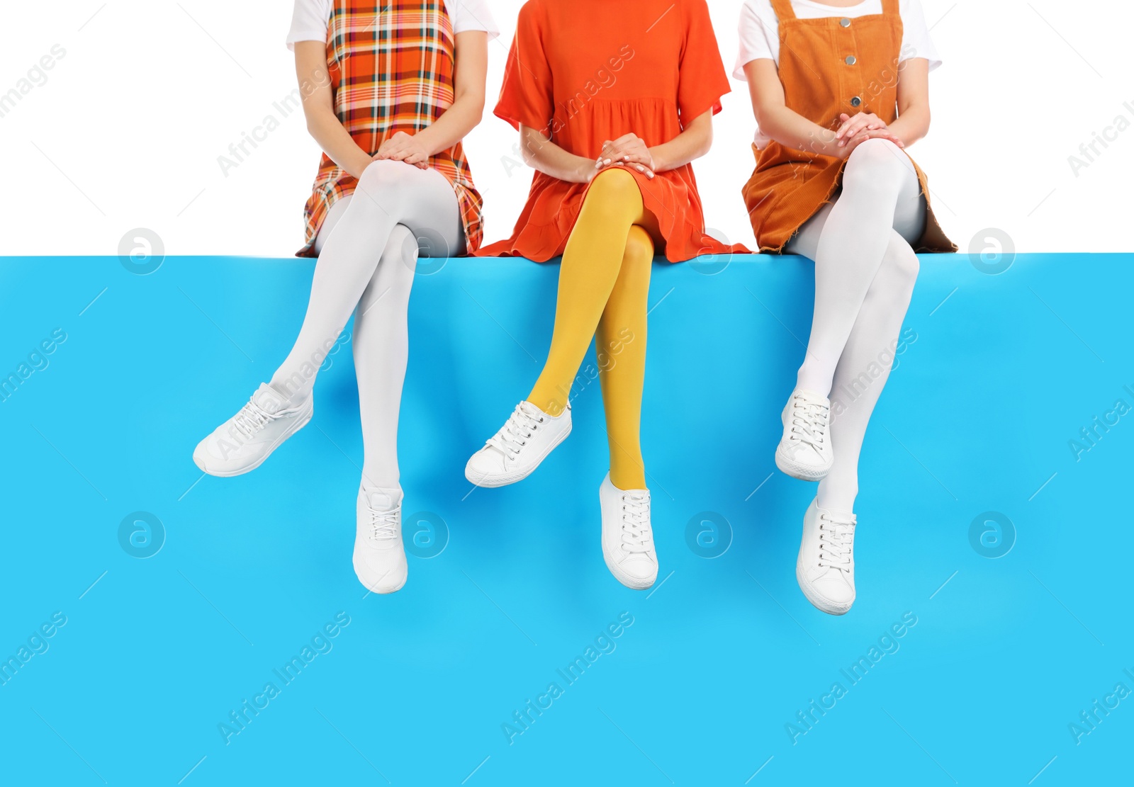 Photo of Group of women wearing colorful tights and stylish shoes sitting on color background, closeup