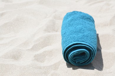 Photo of Rolled blue towel on sandy beach, space for text
