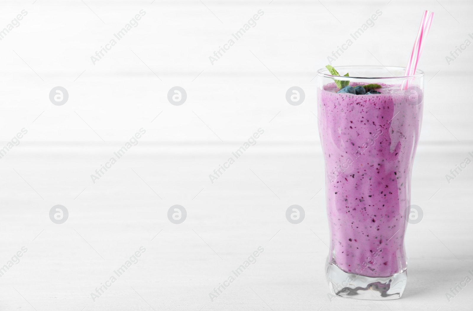 Photo of Glass of tasty blueberry smoothie on white wooden table, space for text