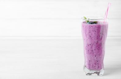 Glass of tasty blueberry smoothie on white wooden table, space for text