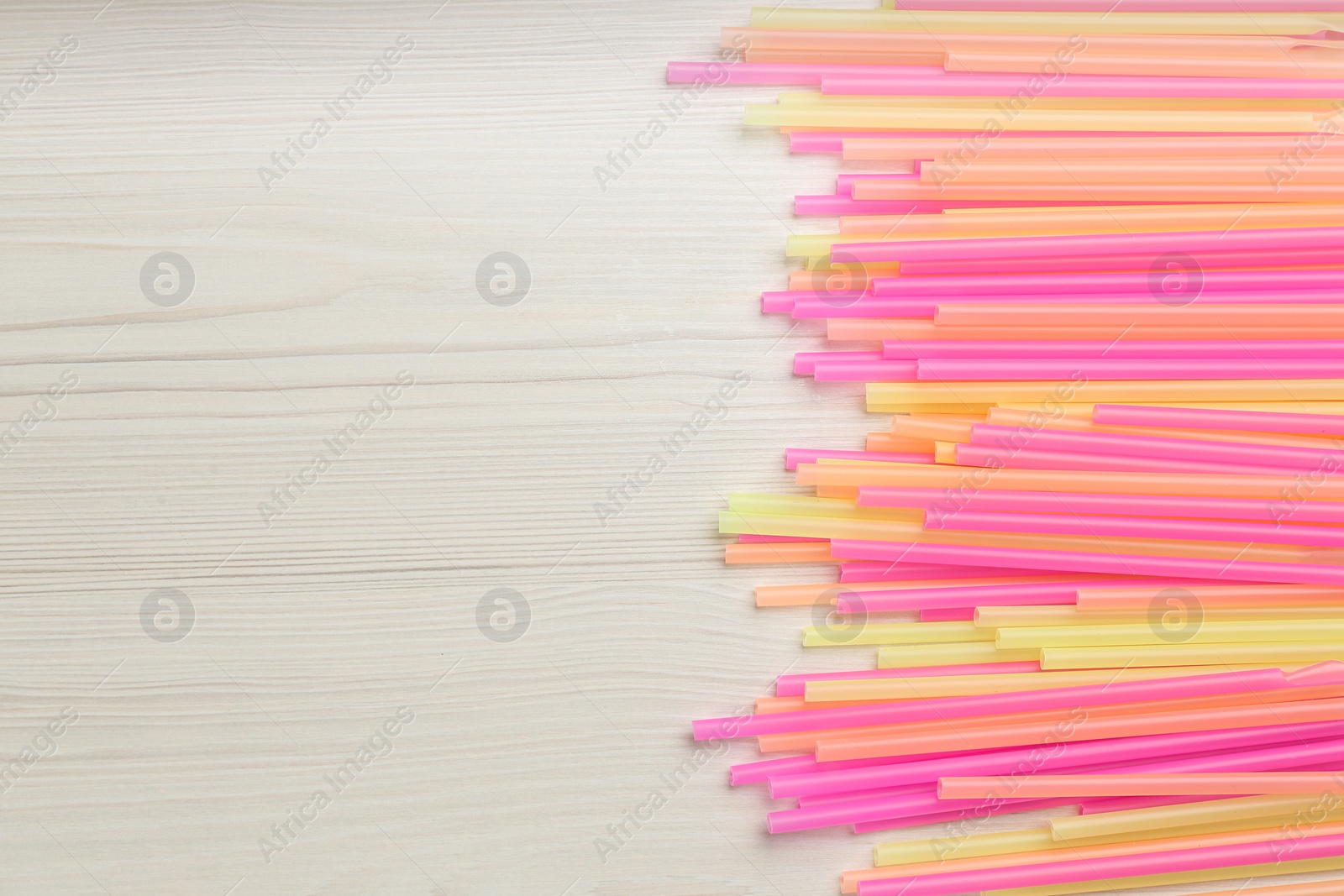 Photo of Colorful plastic drinking straws on white wooden table, flat lay. Space for text