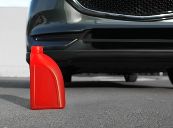 Red canister with motor oil near car on asphalt road