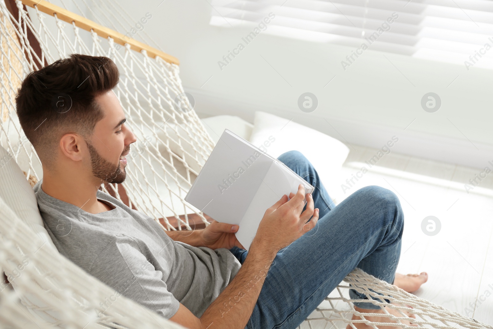 Photo of Young man reading book in hammock at home