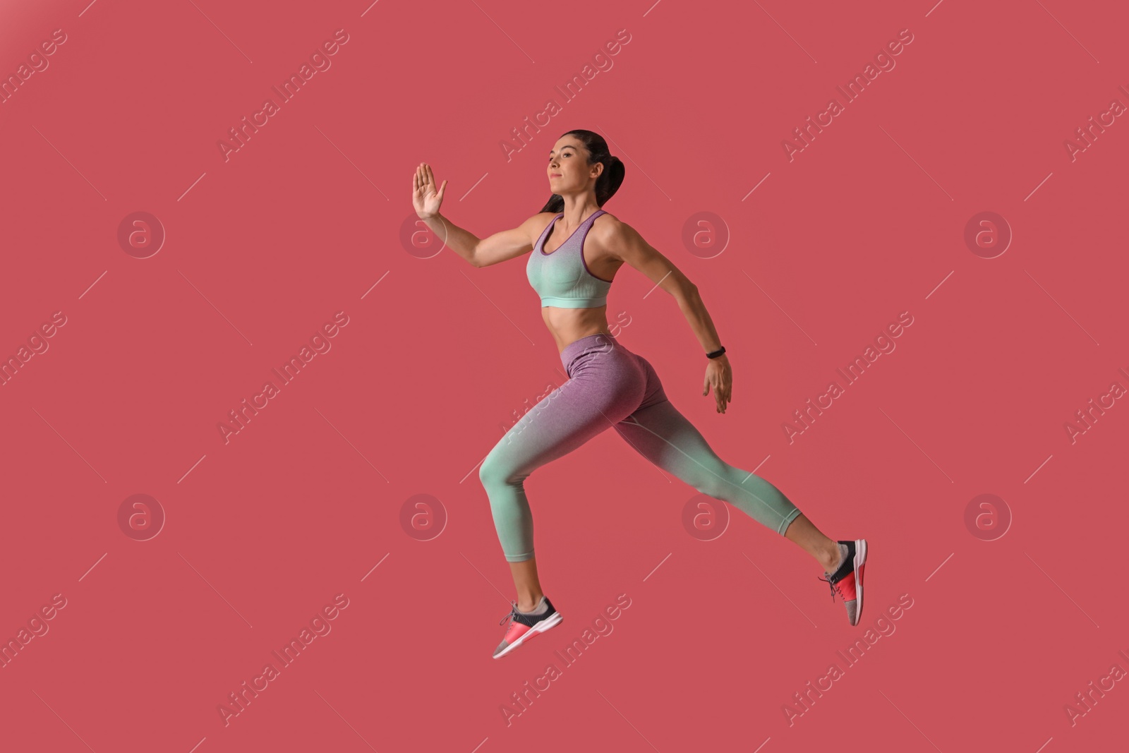 Photo of Athletic young woman running on pink background, side view