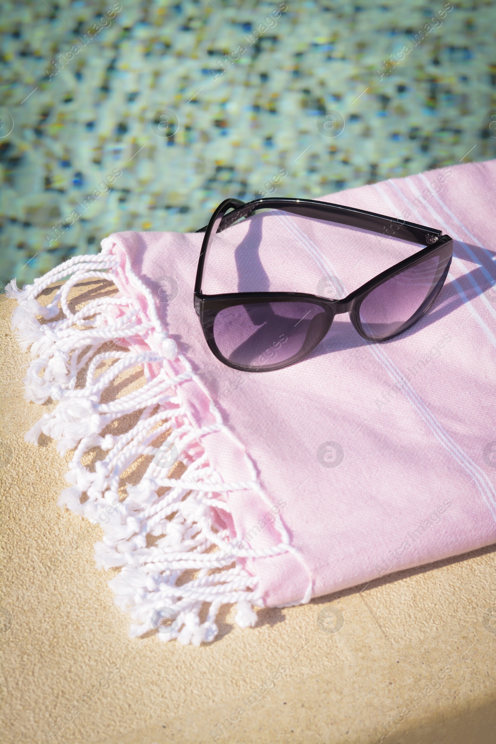 Photo of Stylish sunglasses and blanket near outdoor pool on sunny day