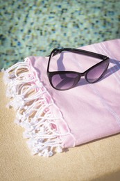 Stylish sunglasses and blanket near outdoor pool on sunny day