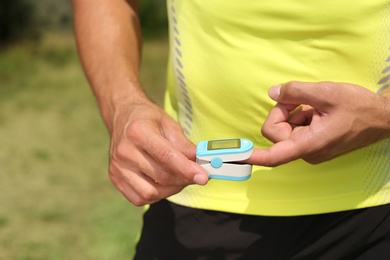 Young man checking pulse with medical device after training outdoors, closeup