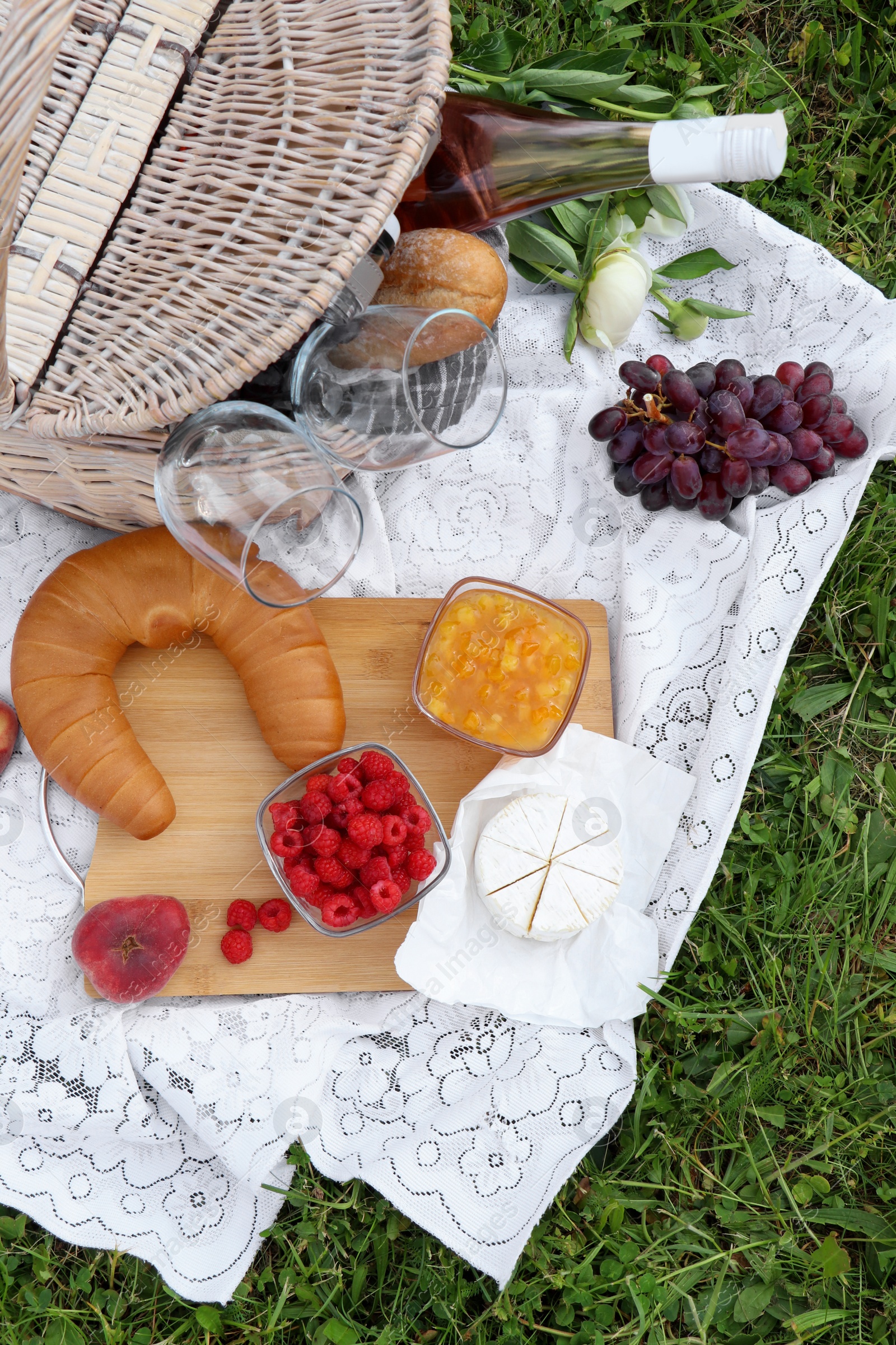 Photo of Picnic blanket with tasty food, flowers and cider on grass outdoors, flat lay