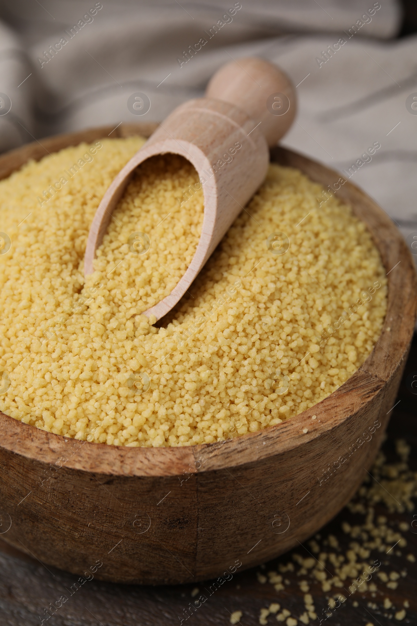 Photo of Bowl and scoop with raw couscous on table, closeup