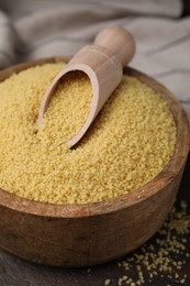 Photo of Bowl and scoop with raw couscous on table, closeup