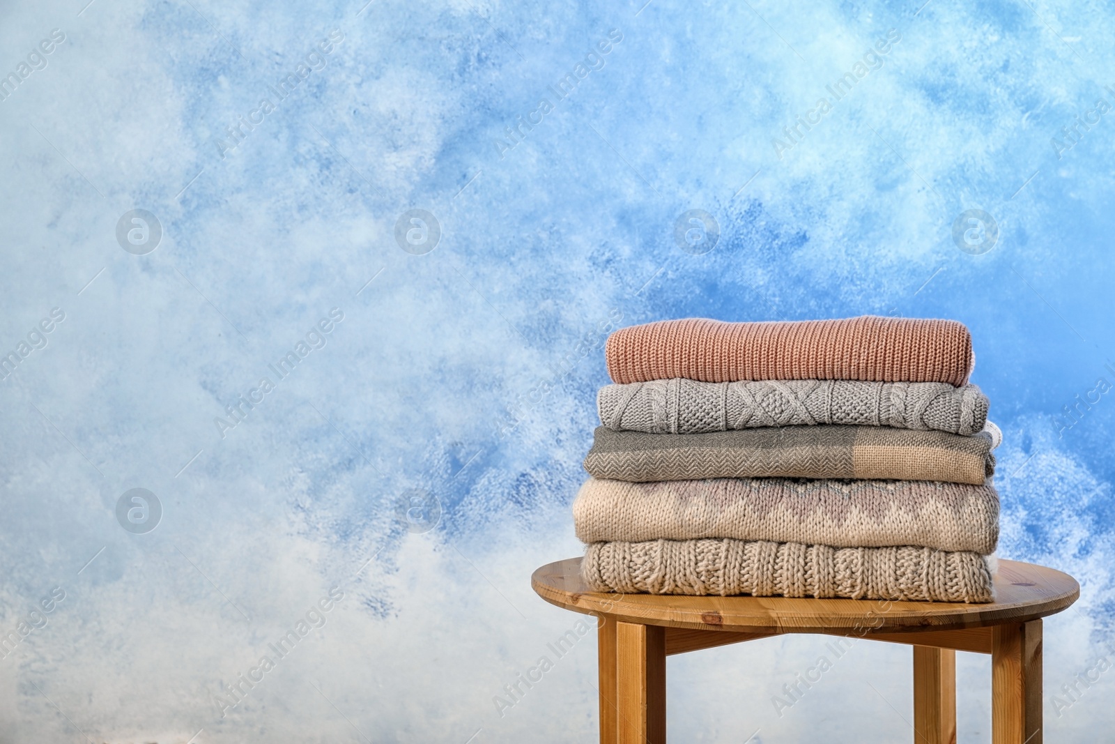 Photo of Stack of warm autumn clothes on stool near color wall. Space for text