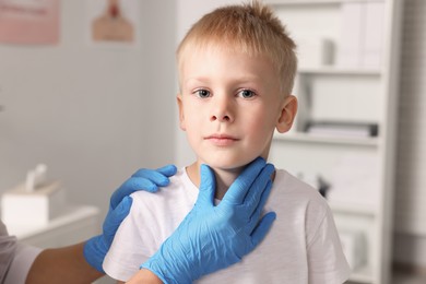 Endocrinologist examining boy's thyroid gland indoors, closeup