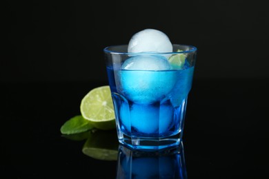 Photo of Delicious cocktail with ice balls and lime on black background